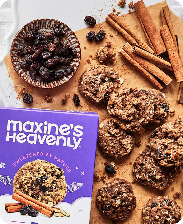 Box of Maxine's Heavenly Cinnamon Oatmeal Raisin Cookies on Cutting Board with Sticks of Cinnamon